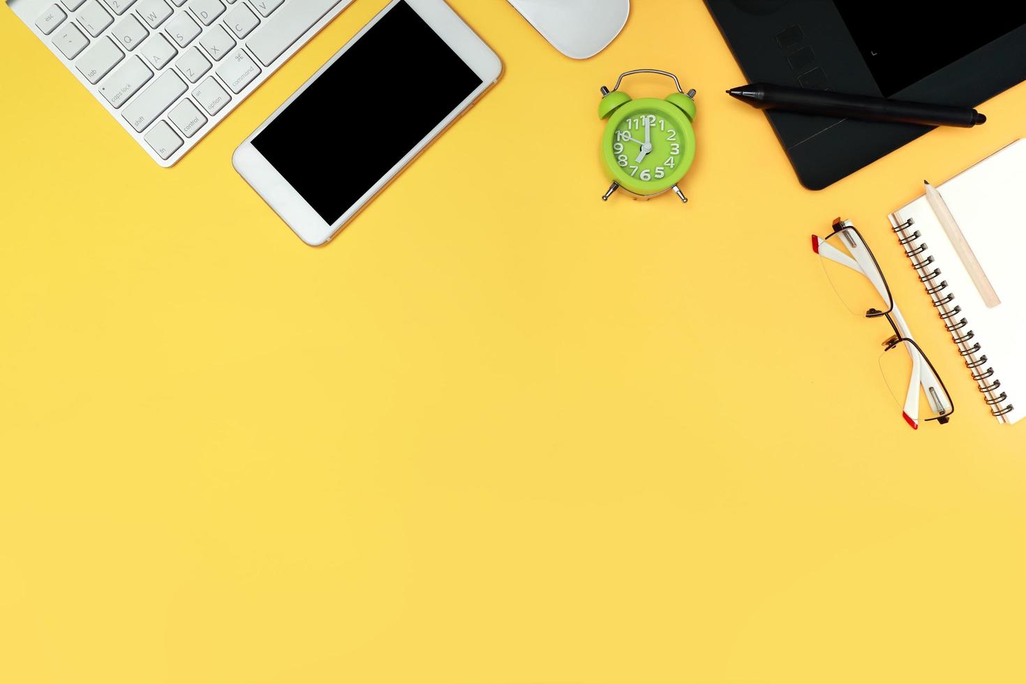 graphic designer desk top view with computer, smart phone, glasses, notebook, and time clock on yellow background photo