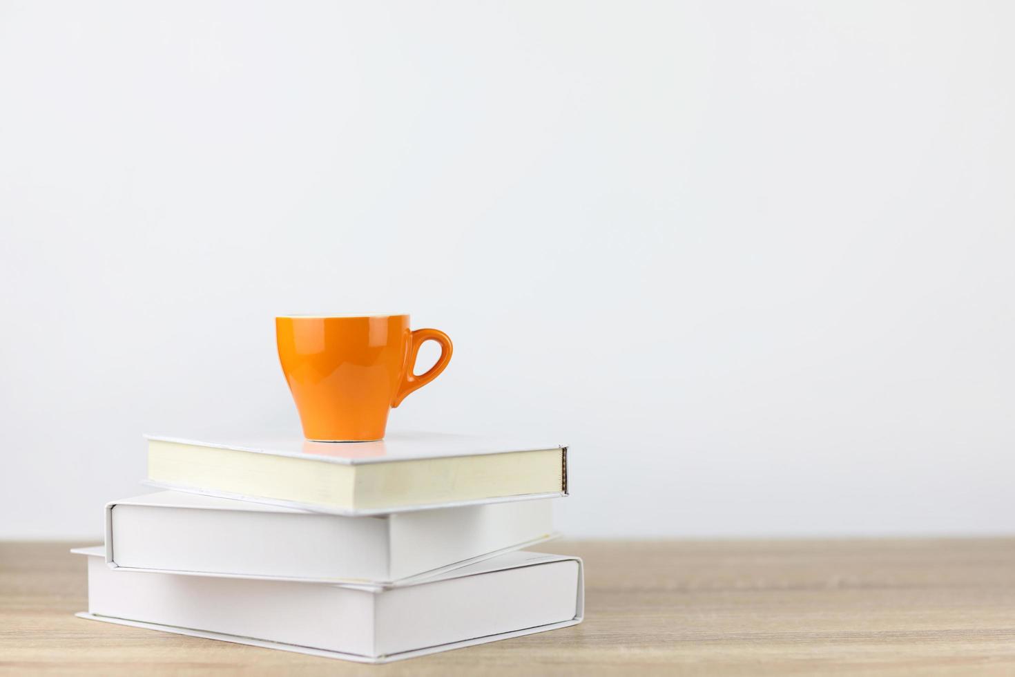 Taza de café con libros sobre un escritorio de madera y fondo blanco. foto