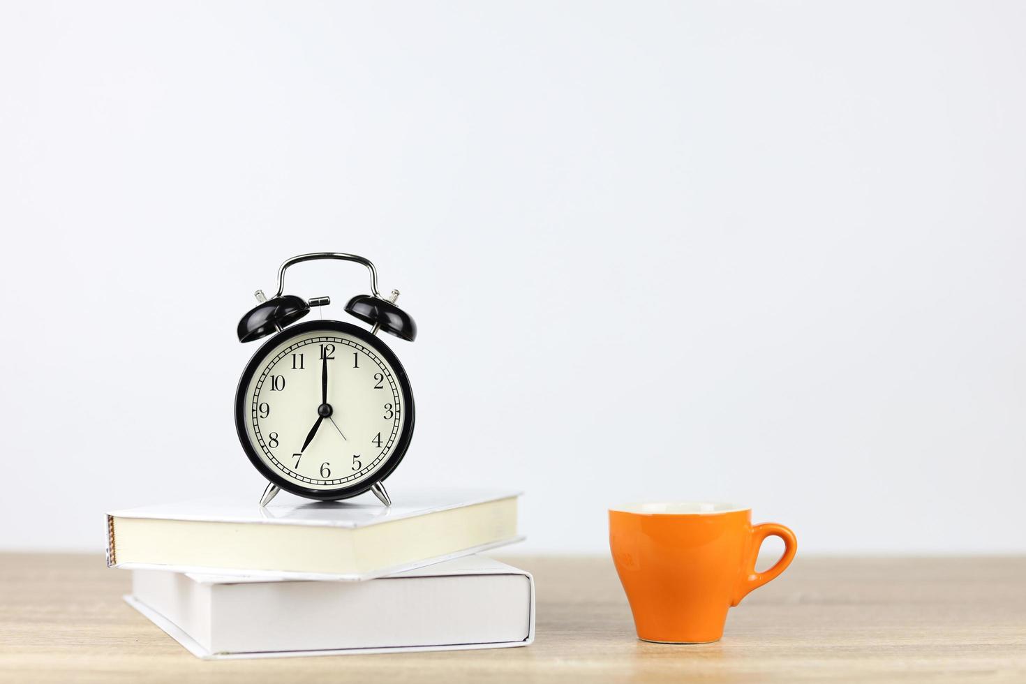 Despertador con libros y taza de café en un escritorio de madera y fondo blanco. foto