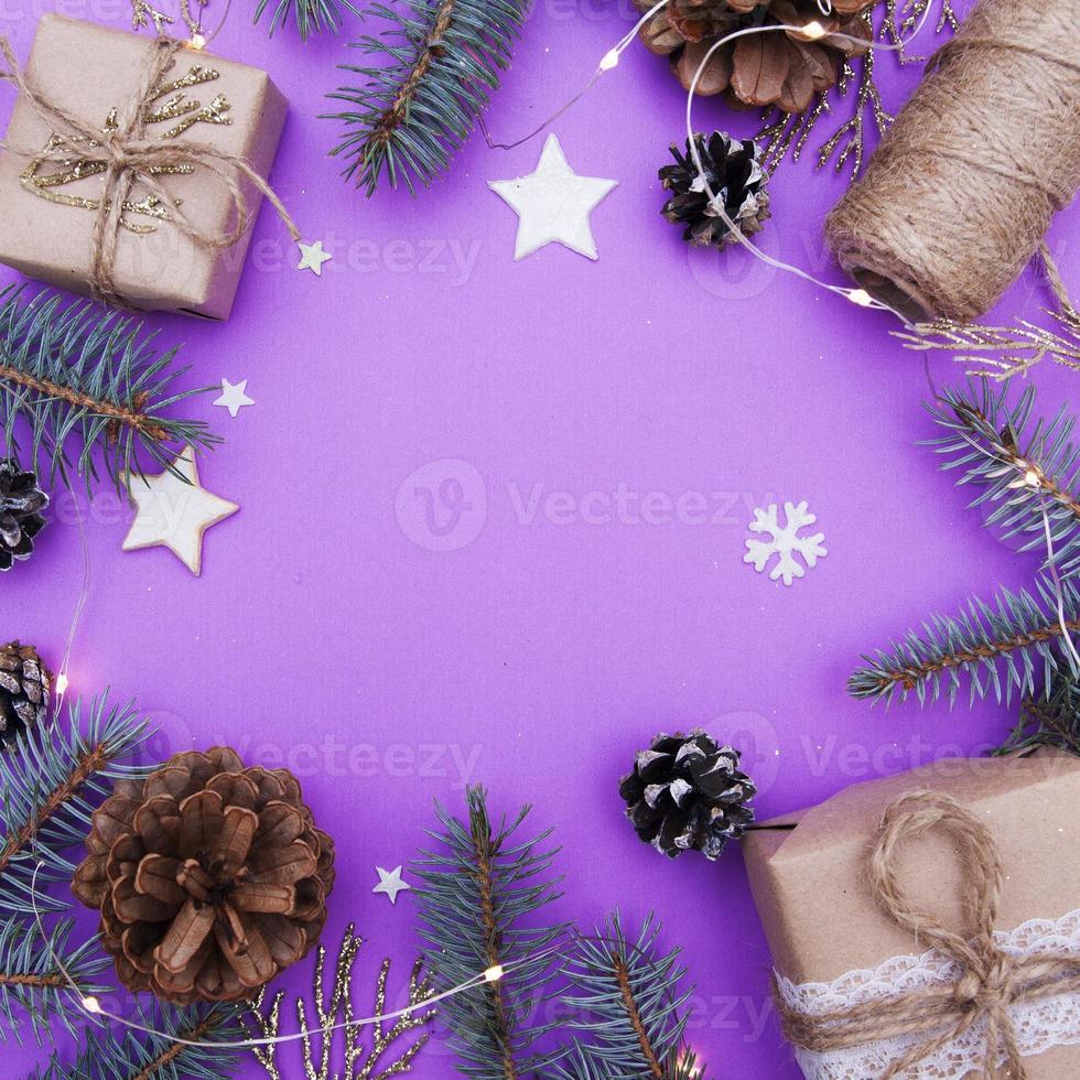 Vista superior de la composición de Navidad. foto de concepto vacaciones de Navidad y año nuevo. ramas de abeto, juguete de árbol de navidad, regalos, cordeles, conos, estrellas, guirnaldas y copos de nieve sobre un fondo morado. endecha plana