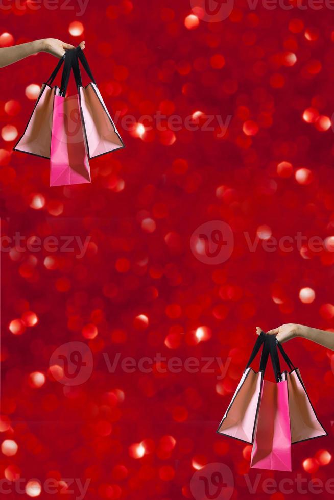 Shopping bags in female hand with holiday sparcles on red boke background photo