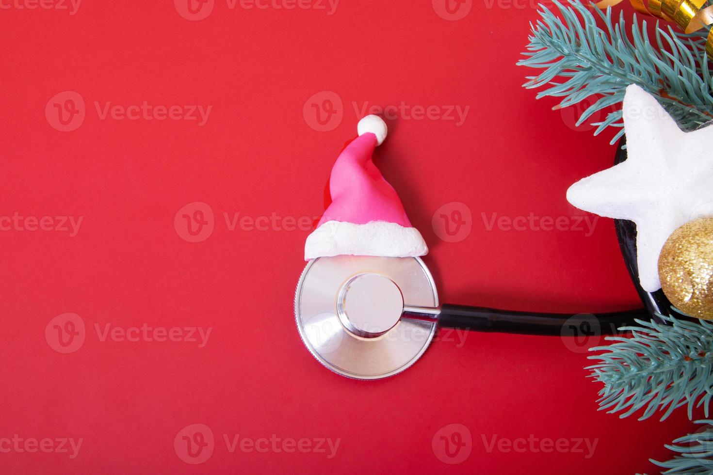 Flat lay medical stethoscope in santa hat and christmas decorations on red background. Medical Christmas concept photo