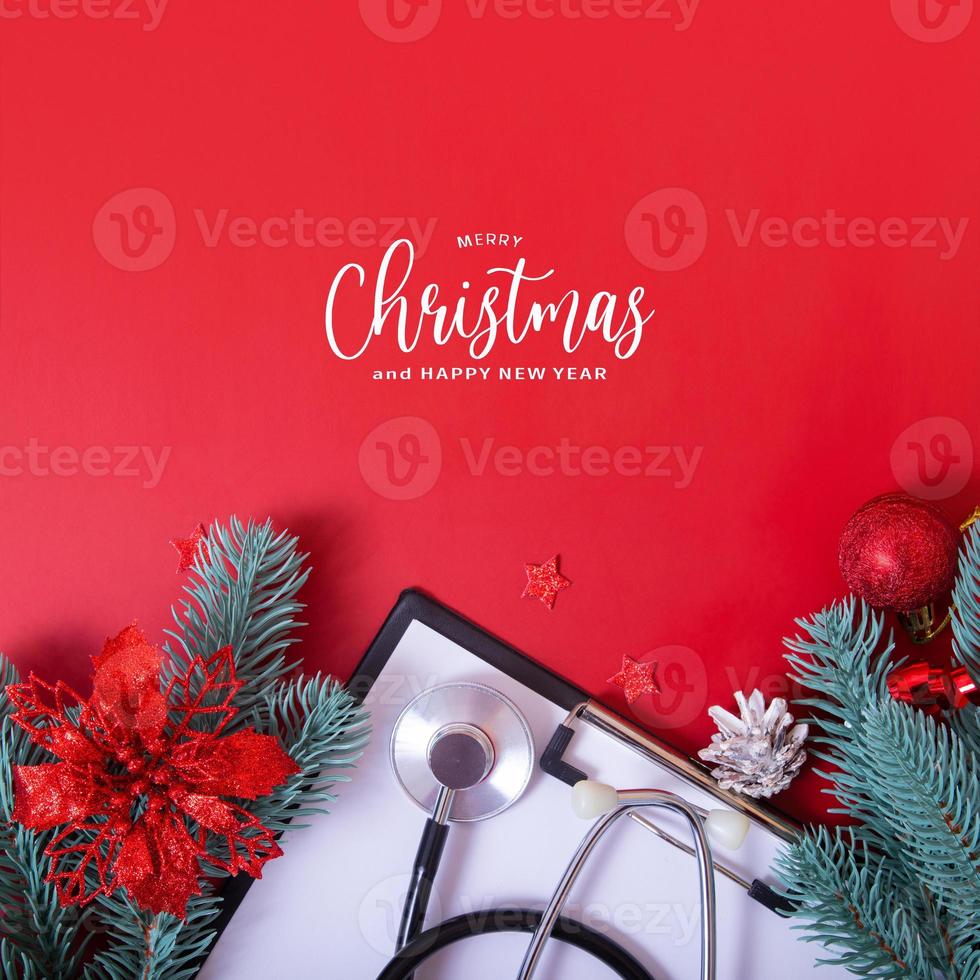 Feliz navidad texto con estetoscopio médico y adornos navideños sobre fondo rojo. foto
