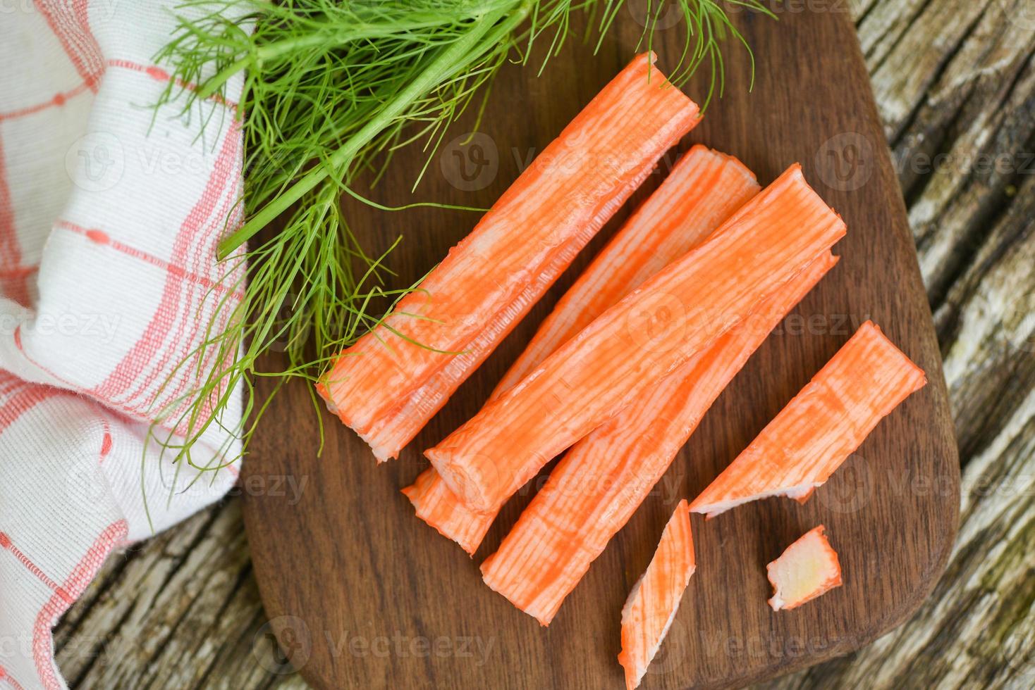 palitos de cangrejo sobre tabla de cortar de madera y vegetales, surimi de palitos de cangrejo fresco listo para comer comida japonesa. foto