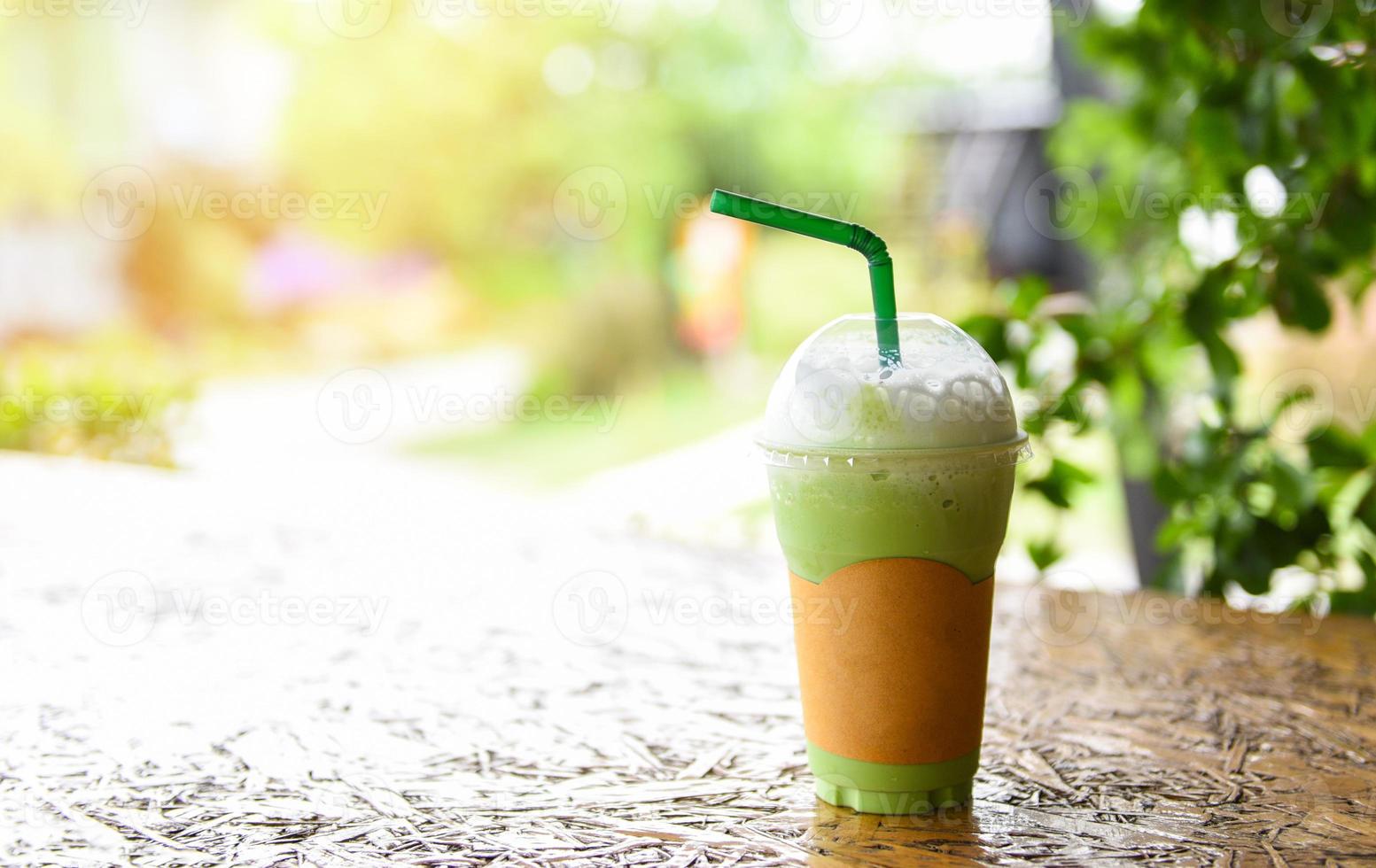 Matcha green tea with milk on plastic glass on the wooden table and nature green background - Green tea smoothie photo