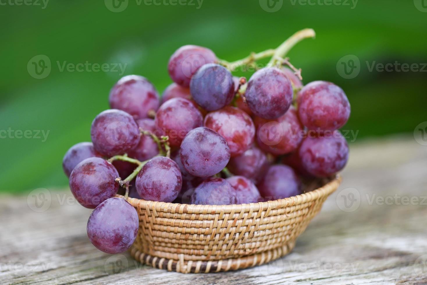 Uva roja madura en canasta sobre fondo verde de madera y natute, fruta fresca de uva. foto