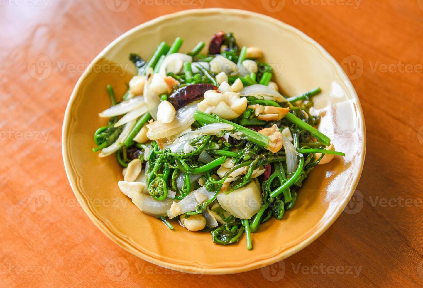 Verduras fritas - salteado de helecho paco con nueces de macadamia en la parte superior de la placa blanca, comida sana foto