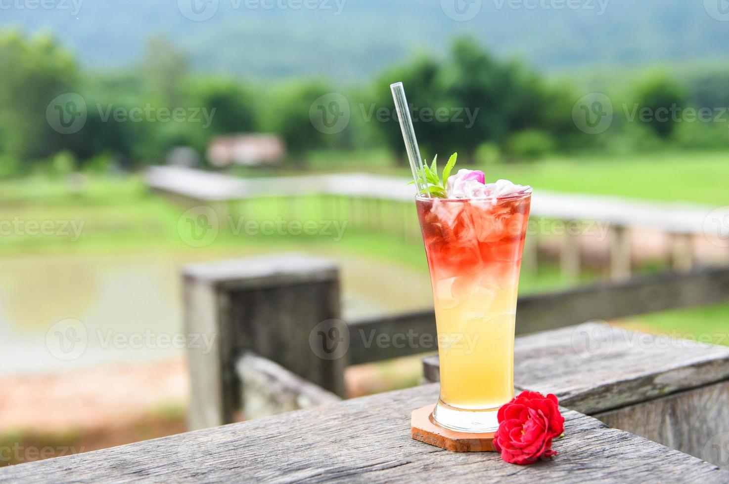 Té helado con un cóctel frío de té de rosas: flores de té hechas de pétalos de rosa de té en un vaso sobre la mesa de madera y la naturaleza de fondo verde foto