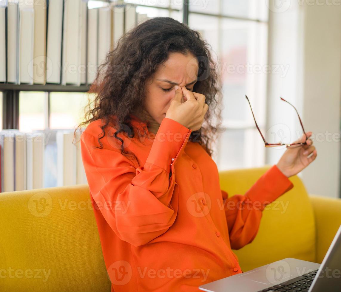 Mujer latina que trabaja con el portátil en el sofá con sensación de cansancio foto