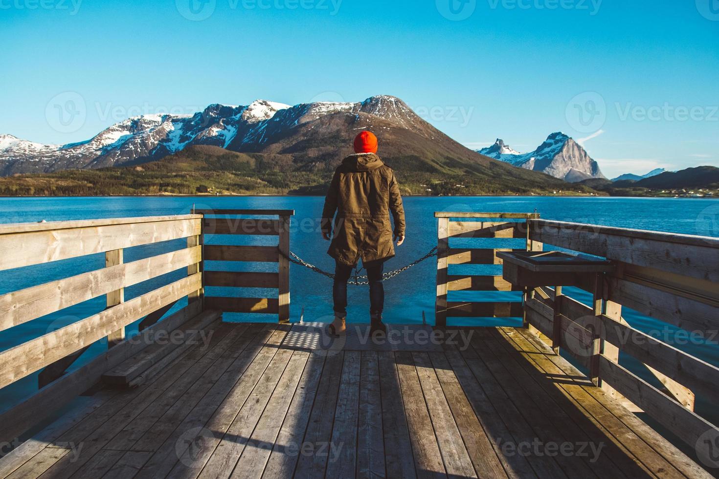 Traveler man stands on wooden pier on background of lake and mountains photo