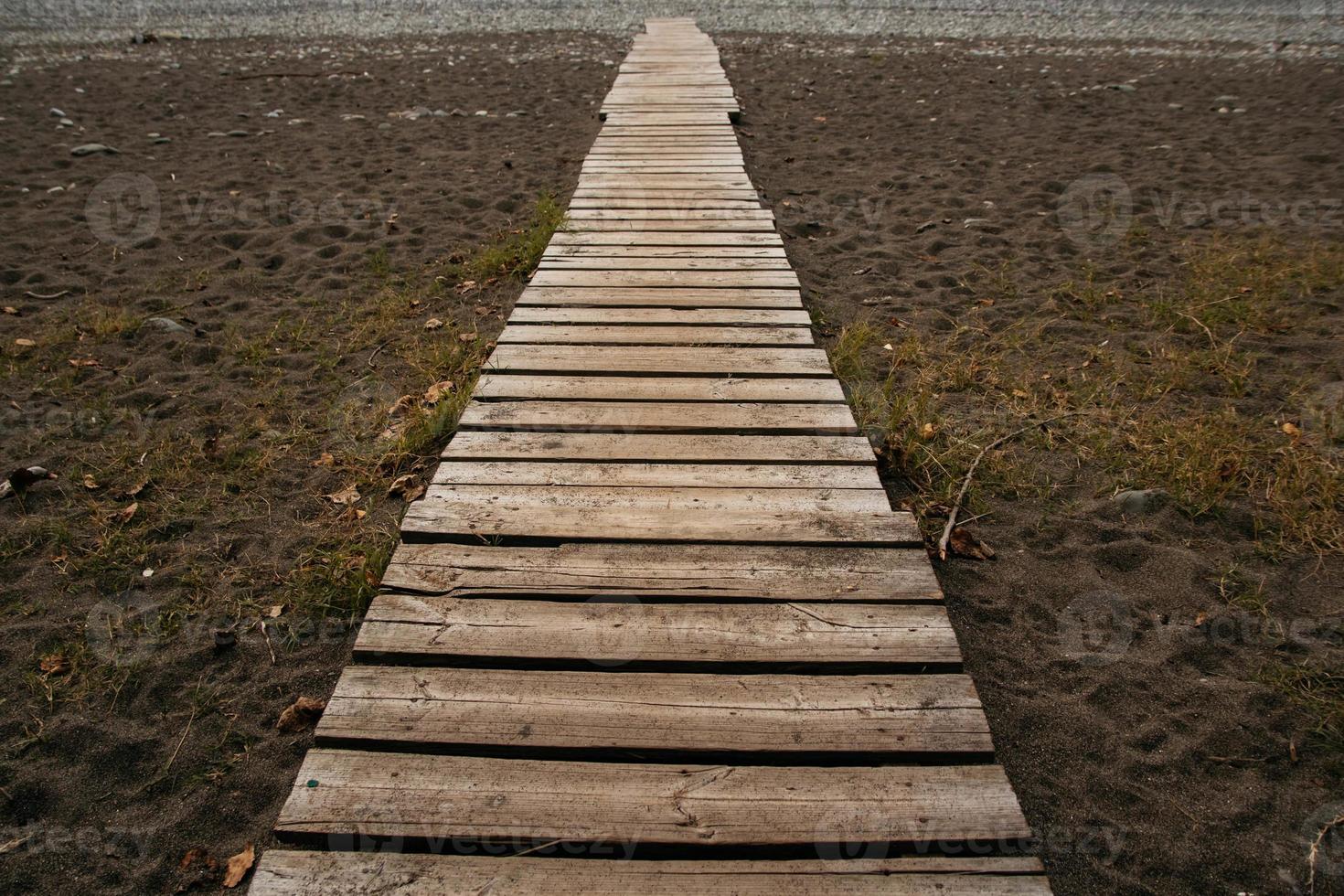 Wooden path on the sandy beach. Beach boardwalk with sand texture background photo