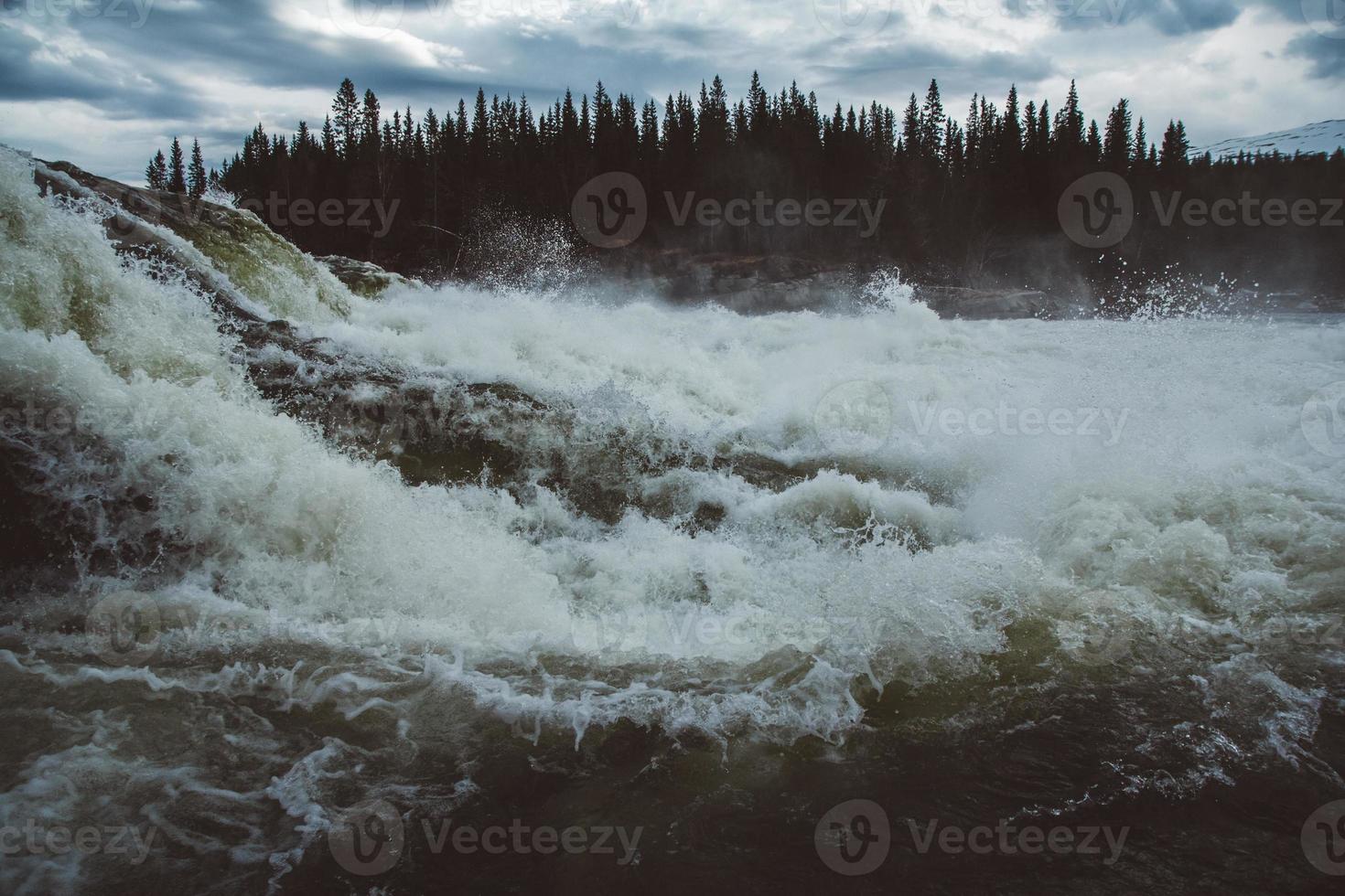 Waves and splashes of mountain river on background of forest and dramatic sky. Forest river water landscape photo