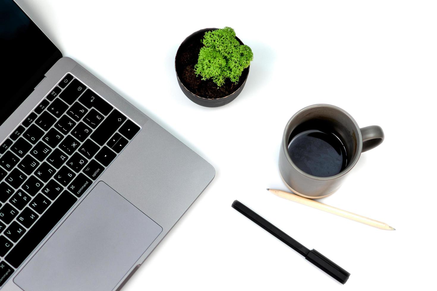 mesa de escritorio de oficina blanca de vista superior con cuaderno en blanco, teclado de computadora portátil, bolígrafo, planta y otros suministros de oficina. con espacio de copia, plano, aislado sobre fondo blanco. taza de café foto