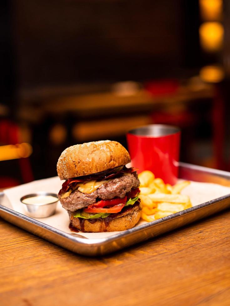 Tasty grilled burger with beef,cheese,bacon and sauce on wooden table with french fries and beer photo