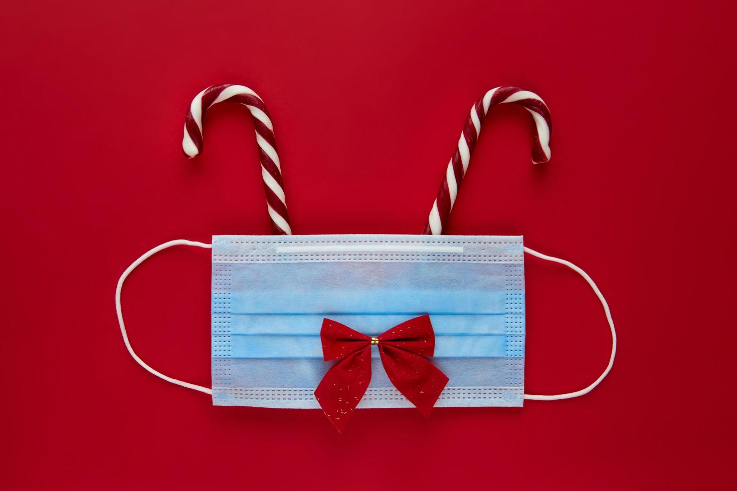 Festive coronavirus reindeer made from face mask and decorations on red background. Flat lay, top view christmas holiday composition. New year wallpaper banner photo