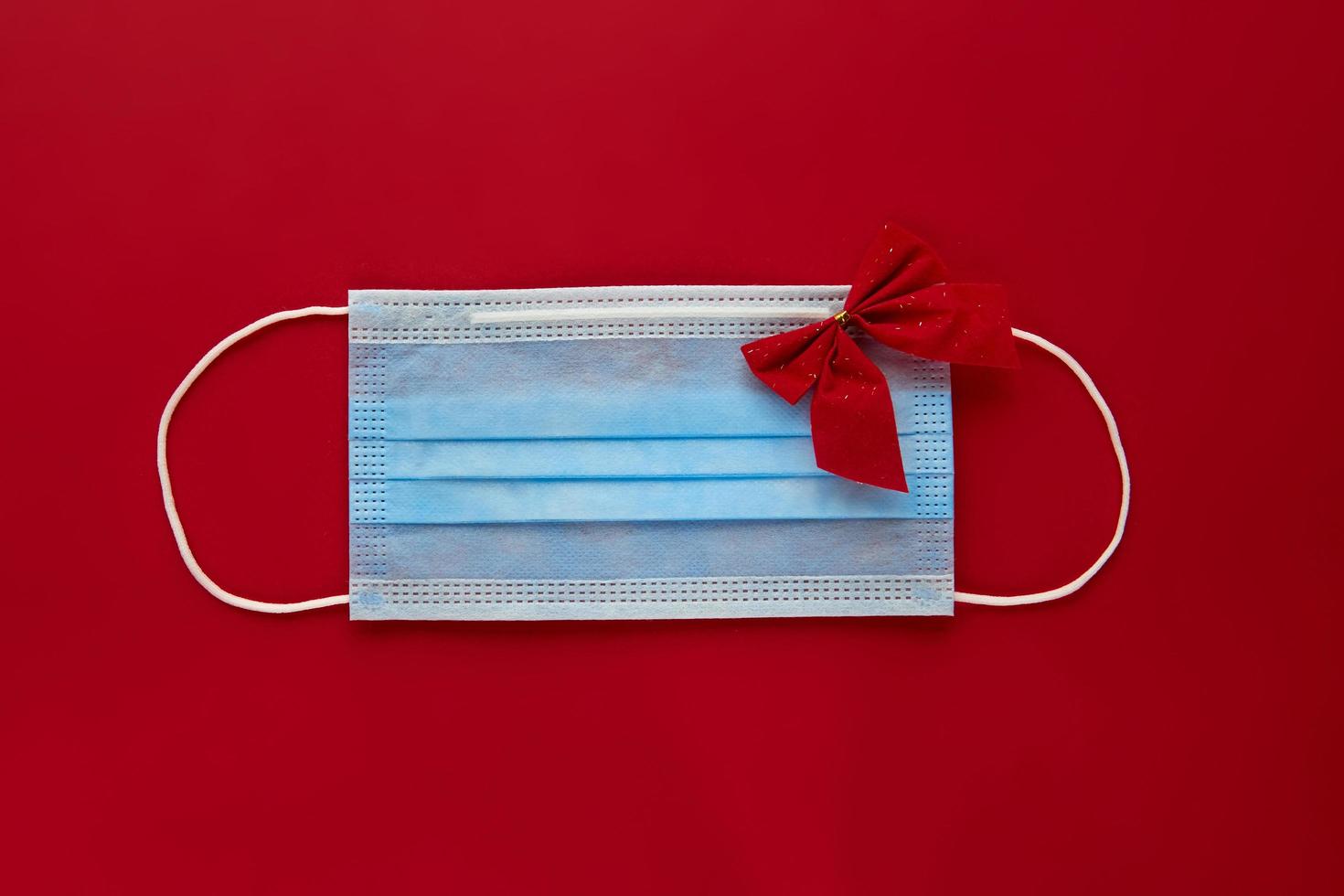 Festive coronavirus face mask with decorations on red background. Flat lay, top view christmas holiday composition. New year wallpaper banner photo