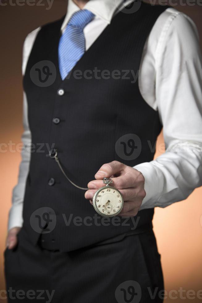 man in elegant suit on orange background holding a pocket watch hanging from his waistcoat photo