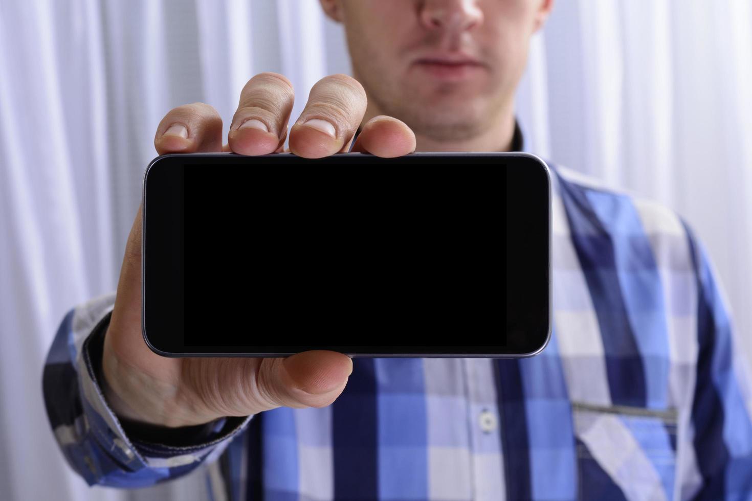 Young man in checkered blue shirt is holding phone with black screen on right hand photo