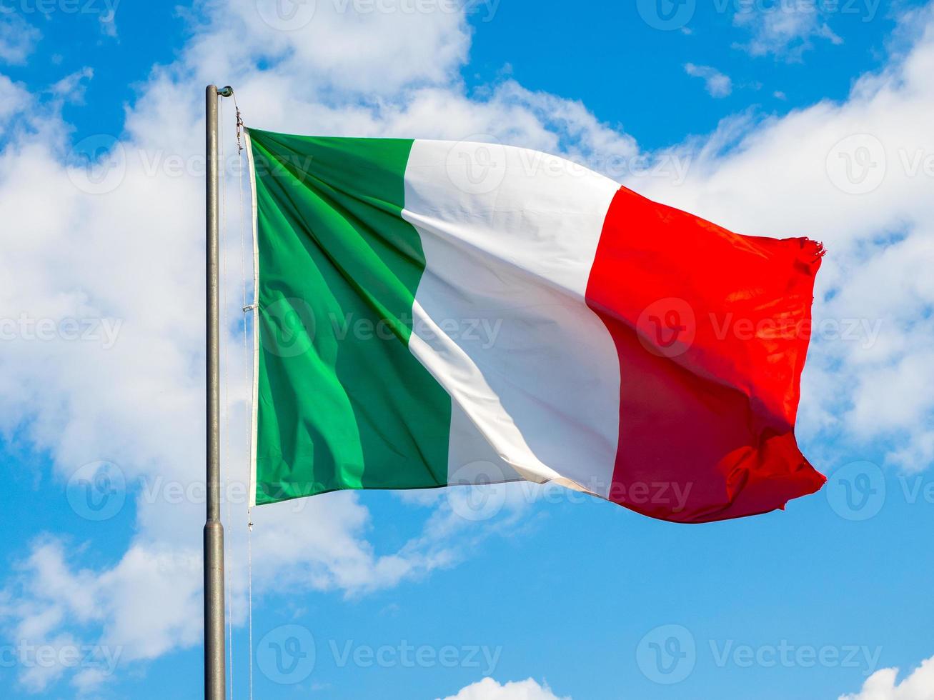 Ondear la bandera italiana con el cielo azul de fondo foto