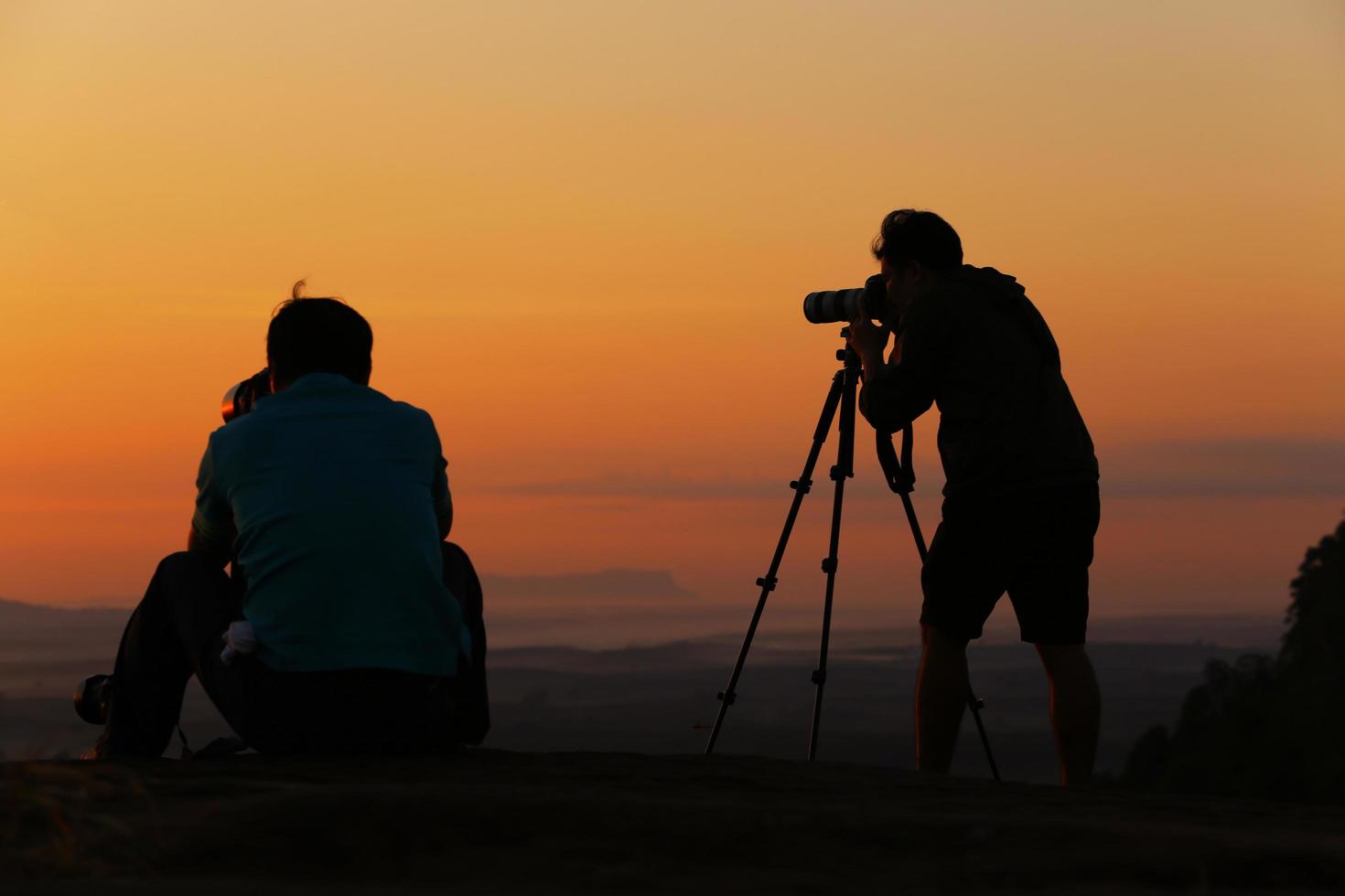 fotógrafa de silueta y amiga de ella disparando al amanecer y viendo el amanecer en la colina. foto