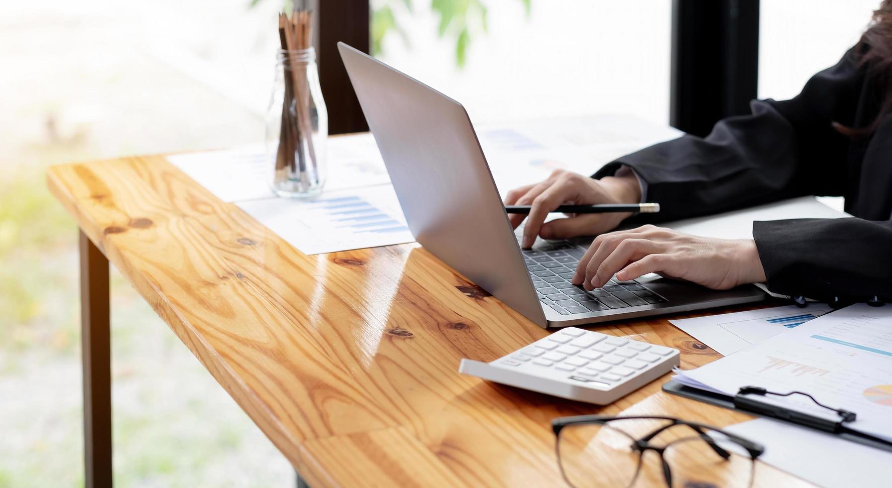 Mujer de negocios de cerca con calculadora y computadora portátil para hacer finanzas matemáticas en un escritorio de madera en la oficina y el fondo de trabajo empresarial, impuestos, contabilidad, estadísticas y concepto de investigación analítica foto