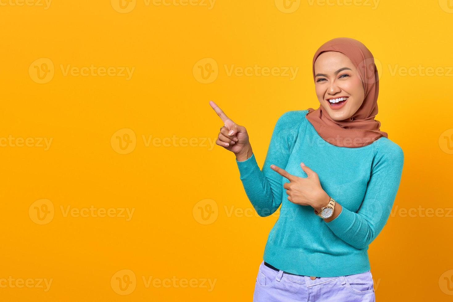 Portrait of smiling young Asian woman pointing finger at copy space on yellow background photo