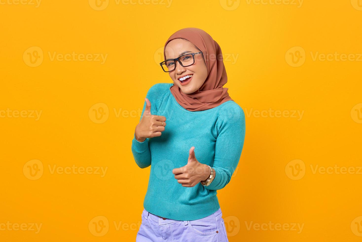 Alegre joven y bella mujer asiática mostrando Thumbs up gesto aislado sobre fondo amarillo foto