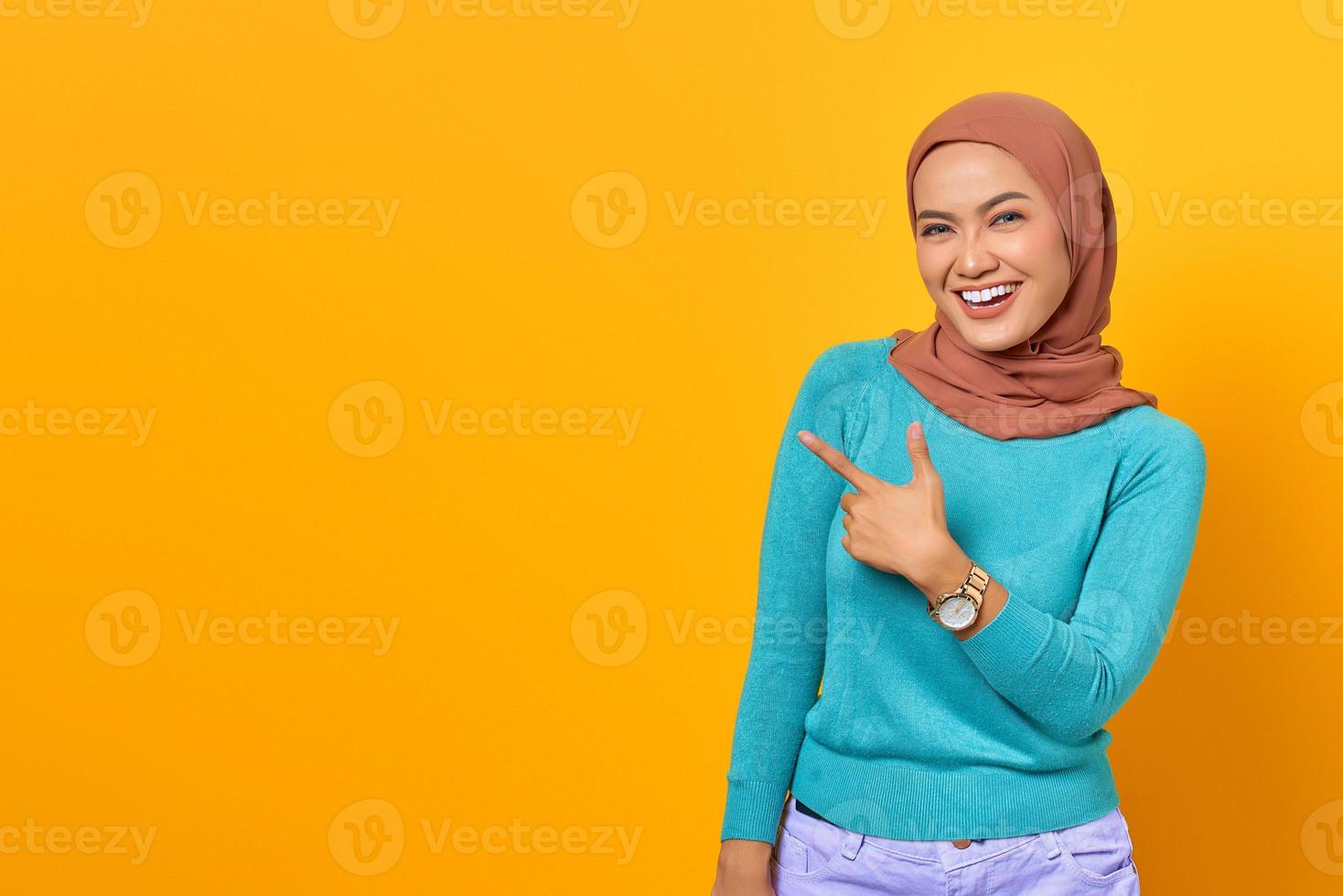 Portrait of smiling young Asian woman pointing finger at copy space on yellow background photo