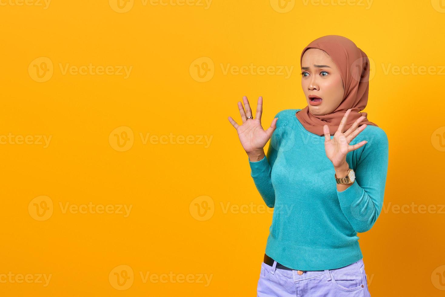 Shocked young Asian woman raised hand with copy space on yellow background photo