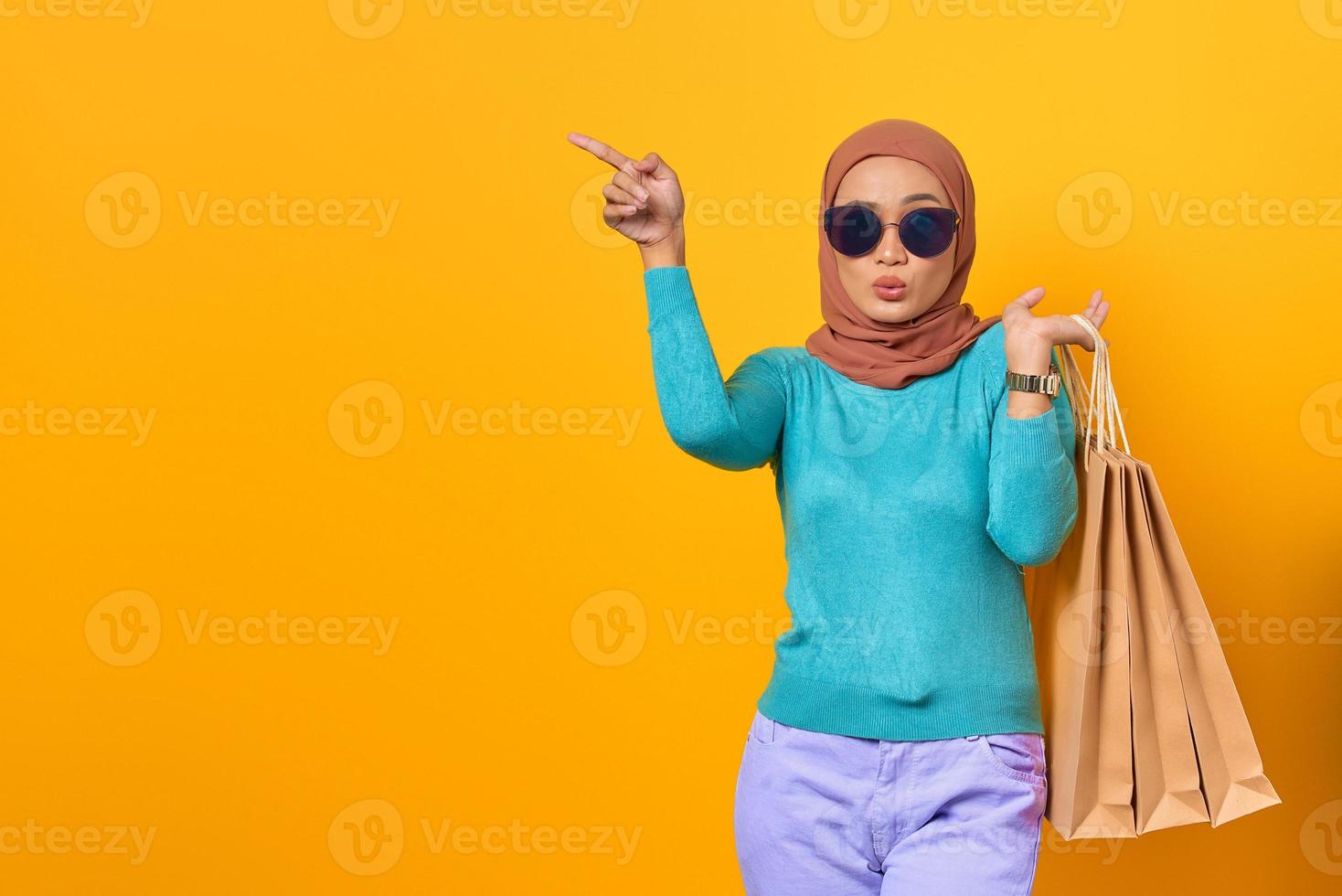 Shocked young Asian woman holding shopping bags and pointing finger at copy space photo