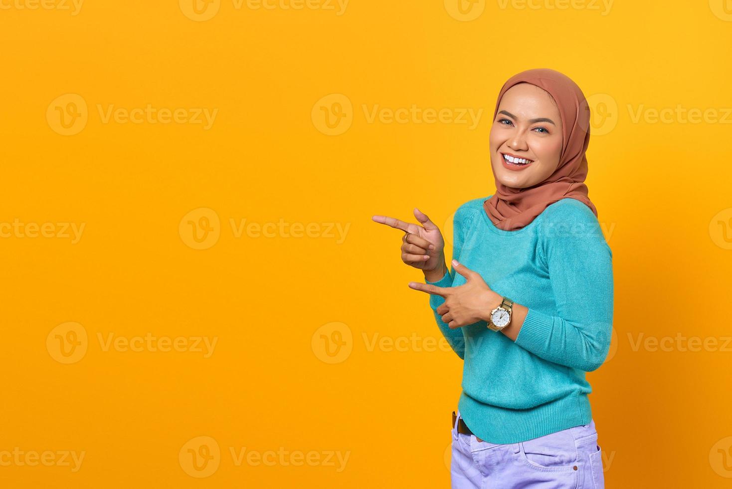 Portrait of smiling young Asian woman pointing finger at copy space on yellow background photo