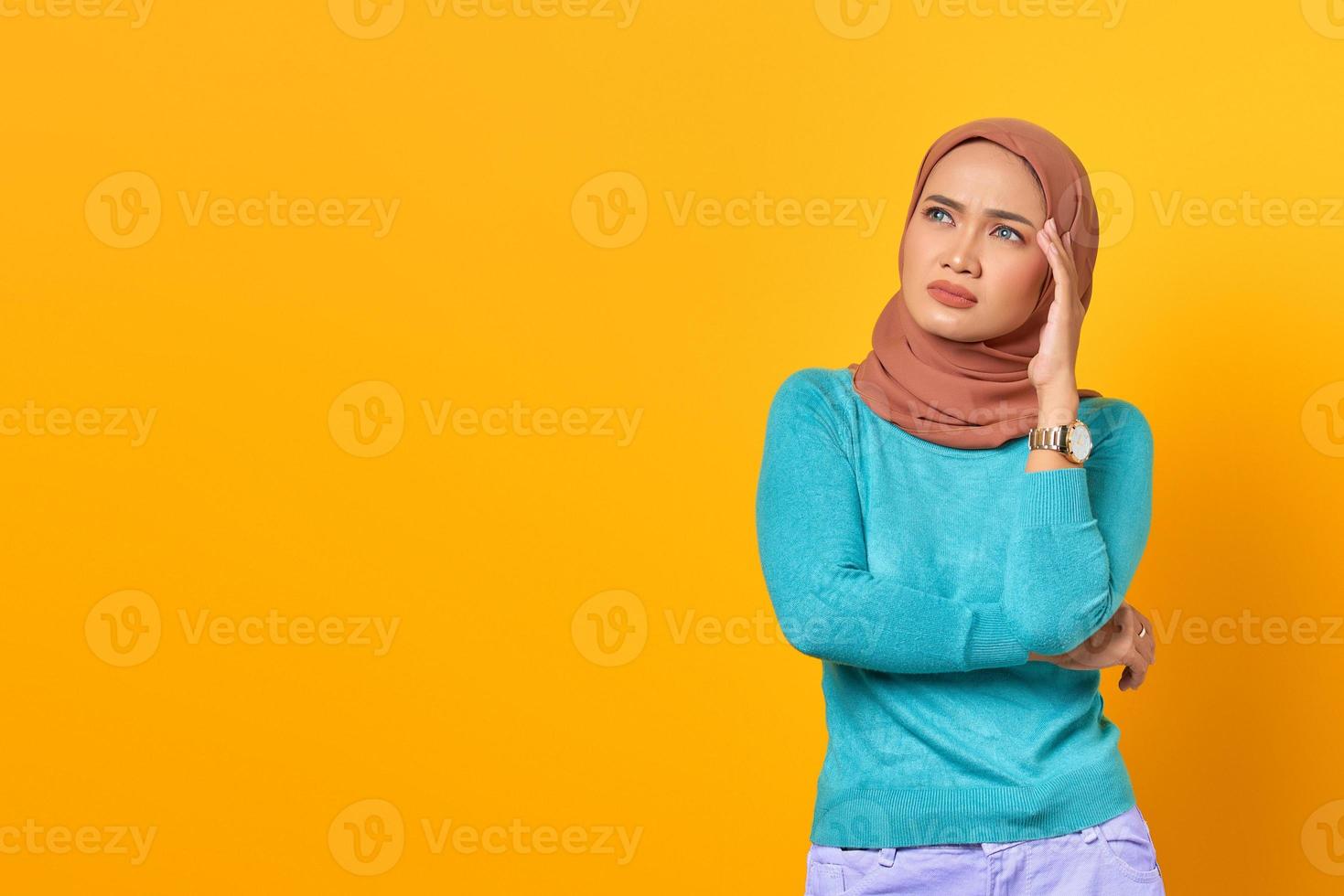 Pensive young Asian woman thinking about something on yellow background photo