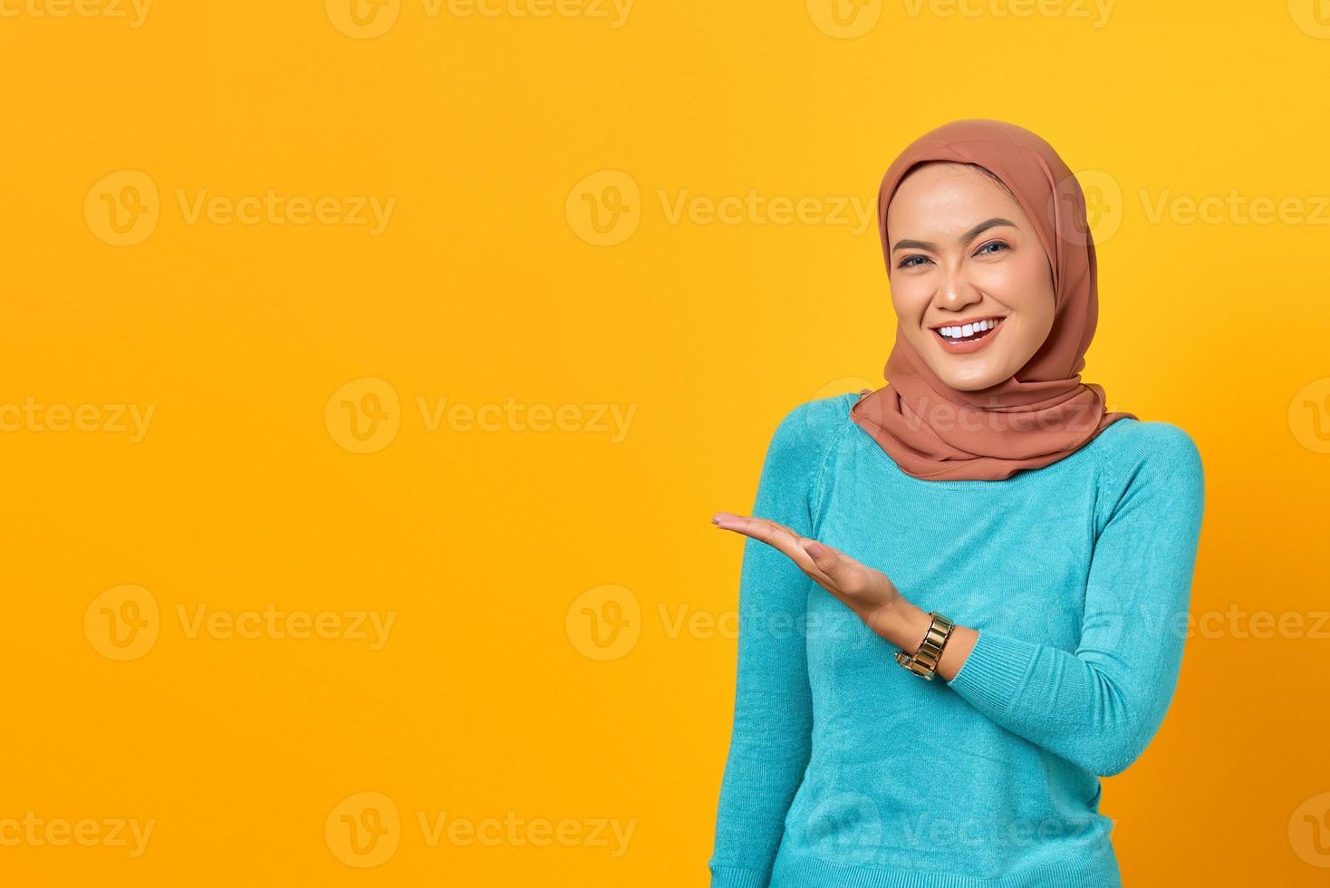 Portrait of smiling young Asian woman showing copy space on palm isolated over yellow background photo