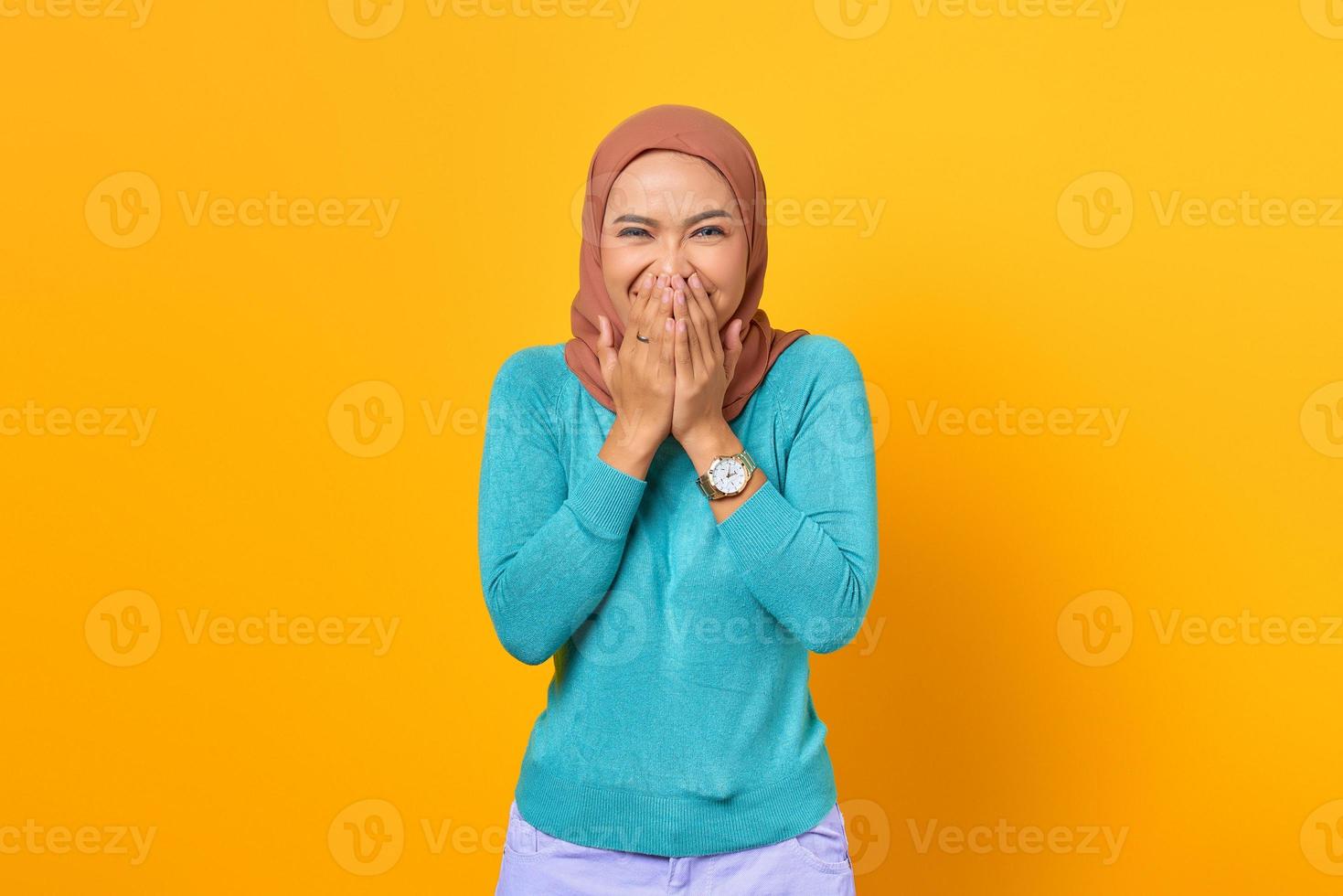 Happy young Asian woman covering mouth with both hands on yellow background photo