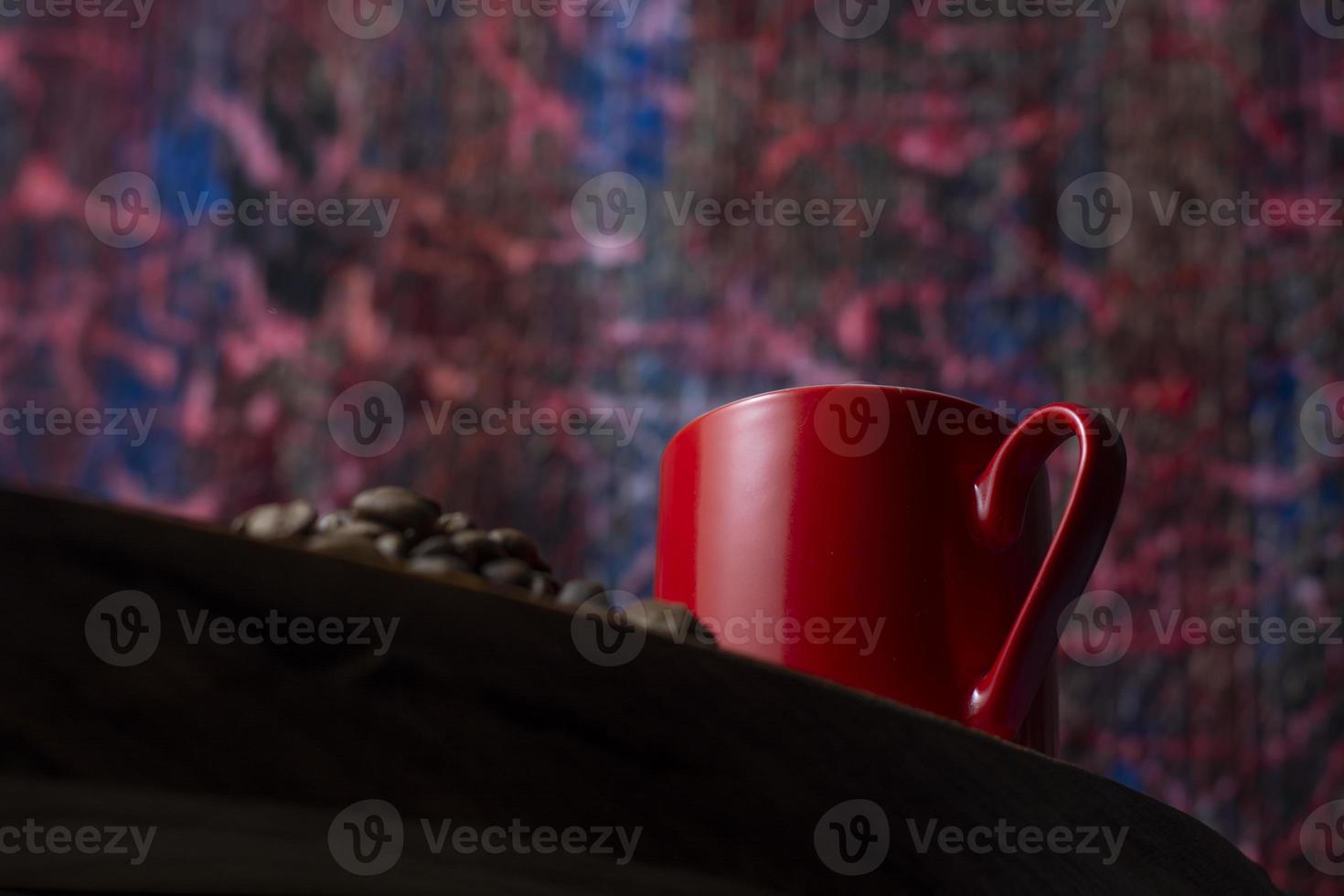 Taza de café rojo sobre la mesa de madera, granos de café, fondo abstracto foto