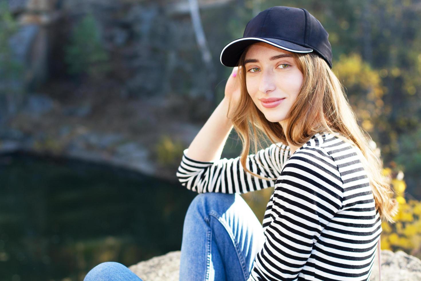 Beautiful young active woman on a background of a beautiful view of the forest and rocks. Girl wearing a cap and casual clothes - active life concept photo