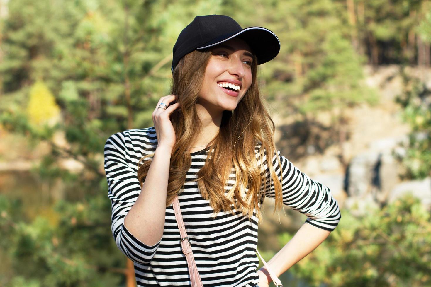 Hermosa joven feliz con dientes blancos y chaqueta negra posando sobre un fondo de bosque salvaje anr montaña foto