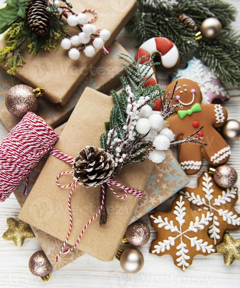 Stylish rustic christmas gifts with pine branches and  decoration on background of golden baubles, pine cones, gingerbread cookies. photo