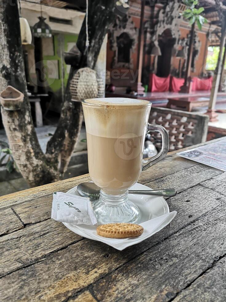 Leche de café en un vaso largo con una galleta sobre una mesa de madera foto