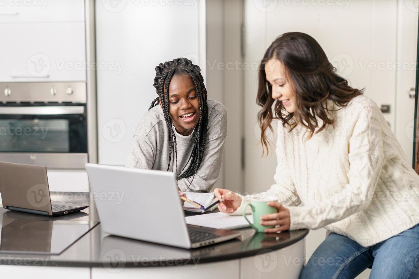 Dos chicas universitarias que estudian juntas en casa con computadoras portátiles mientras beben café foto