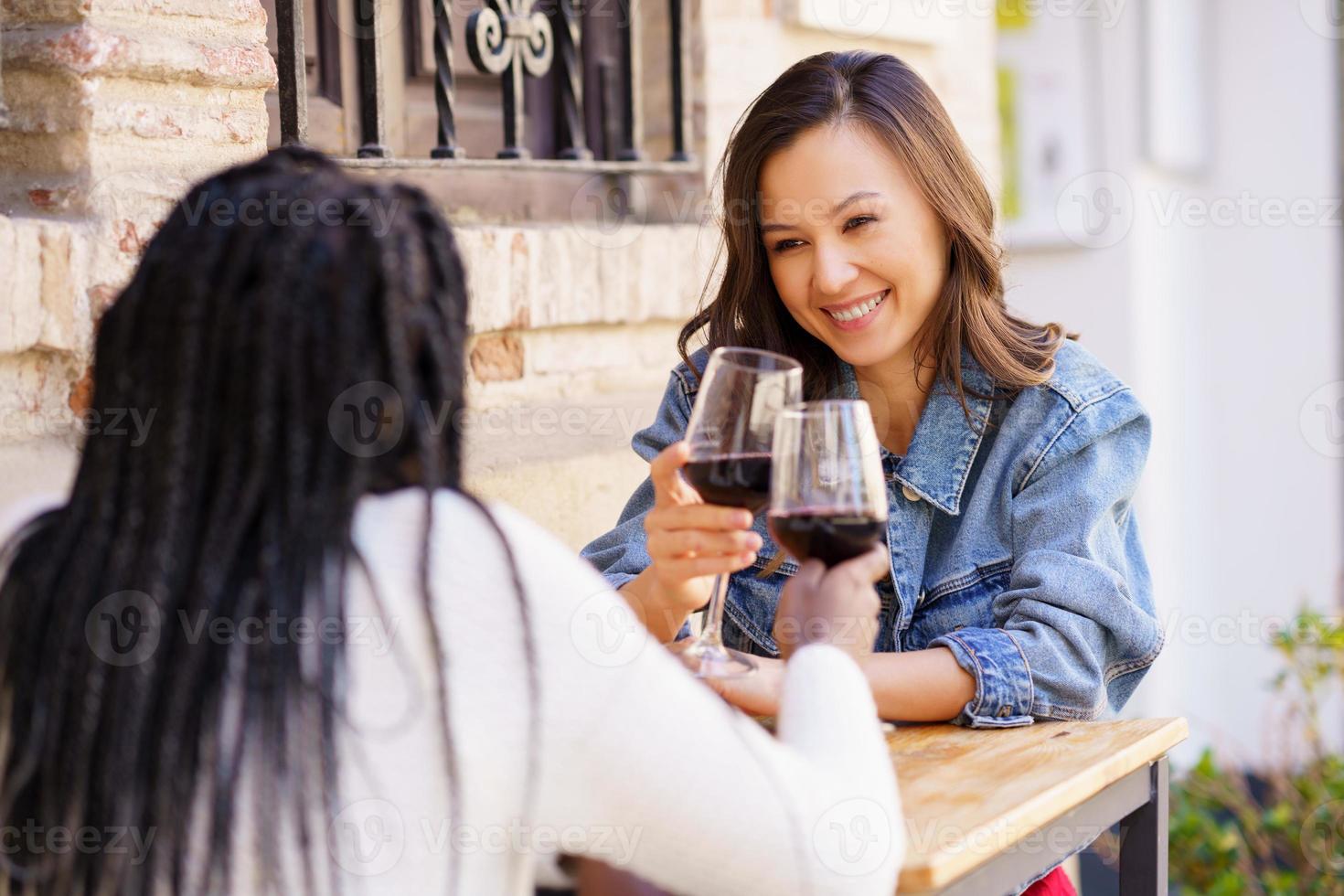 Two women making a toast with red wine sitting at a table outside a bar. photo