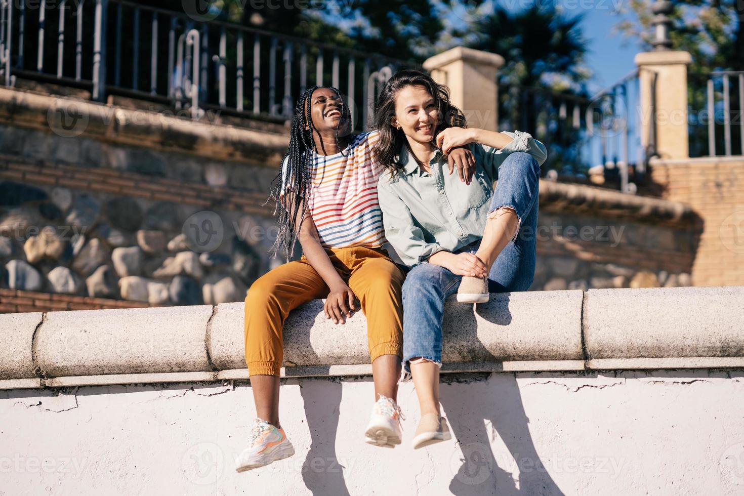 dos amigos divirtiéndose juntos en la calle sentados en una muralla urbana. foto