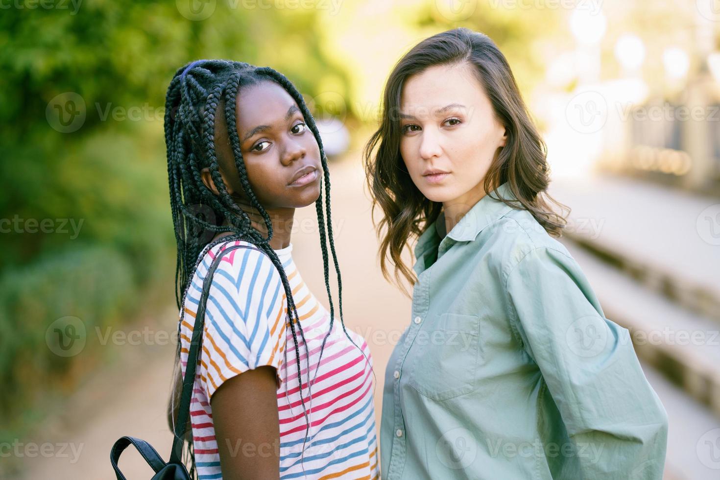 Two young friends looking at camera together on the street. Multiethnic women. photo