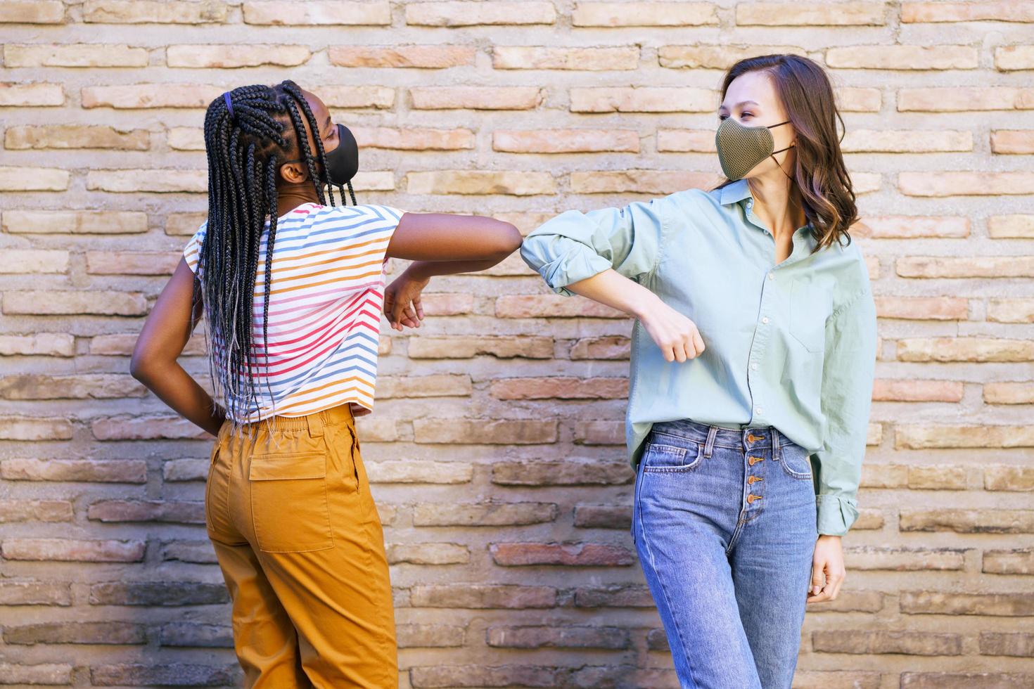 Mujeres jóvenes multiétnicas con máscaras saludándose con los codos foto