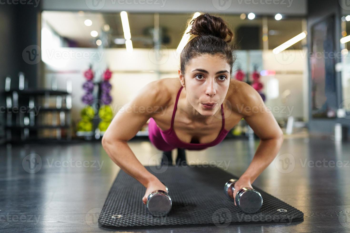 Mujer haciendo ejercicio de flexiones con mancuernas en un entrenamiento físico foto