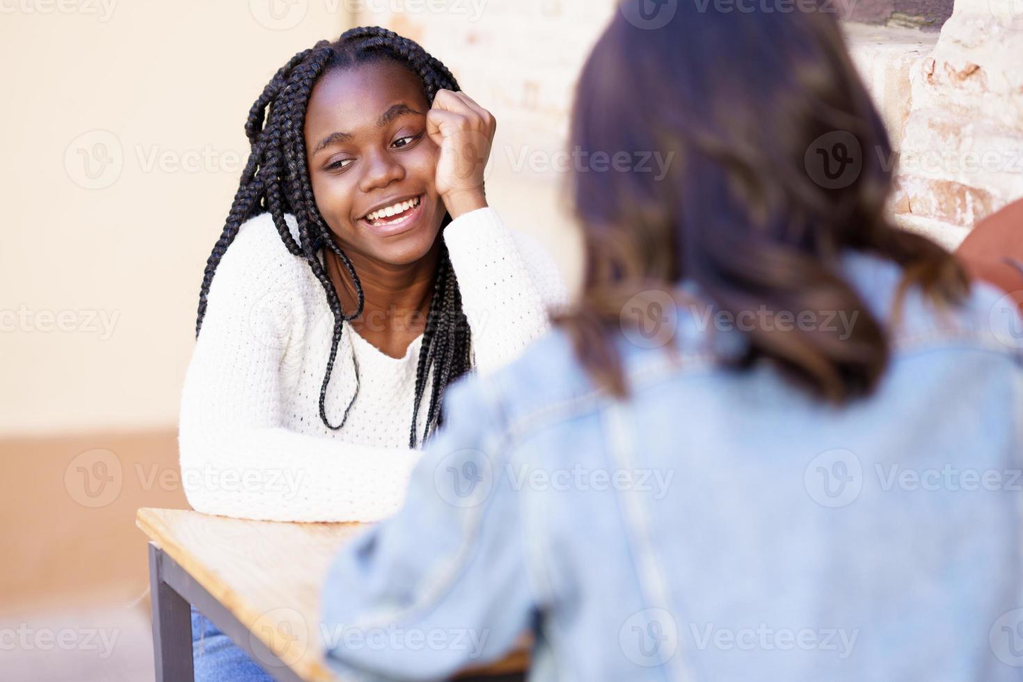 Two multiethnic friends talking sitting at a table outside a bar. photo