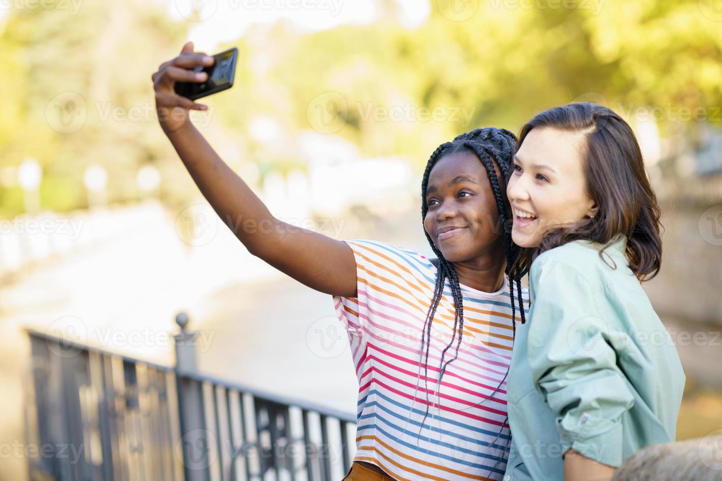 dos amigas multiétnicas haciendo selfie al aire libre. foto