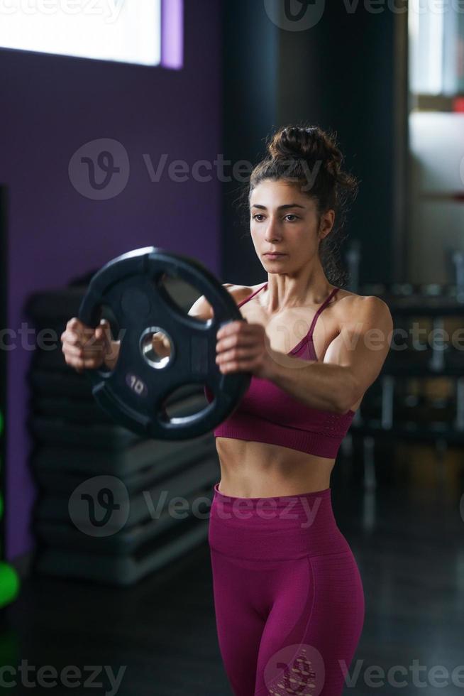 Athletic woman doing triceps push-ups with a barbell plate photo