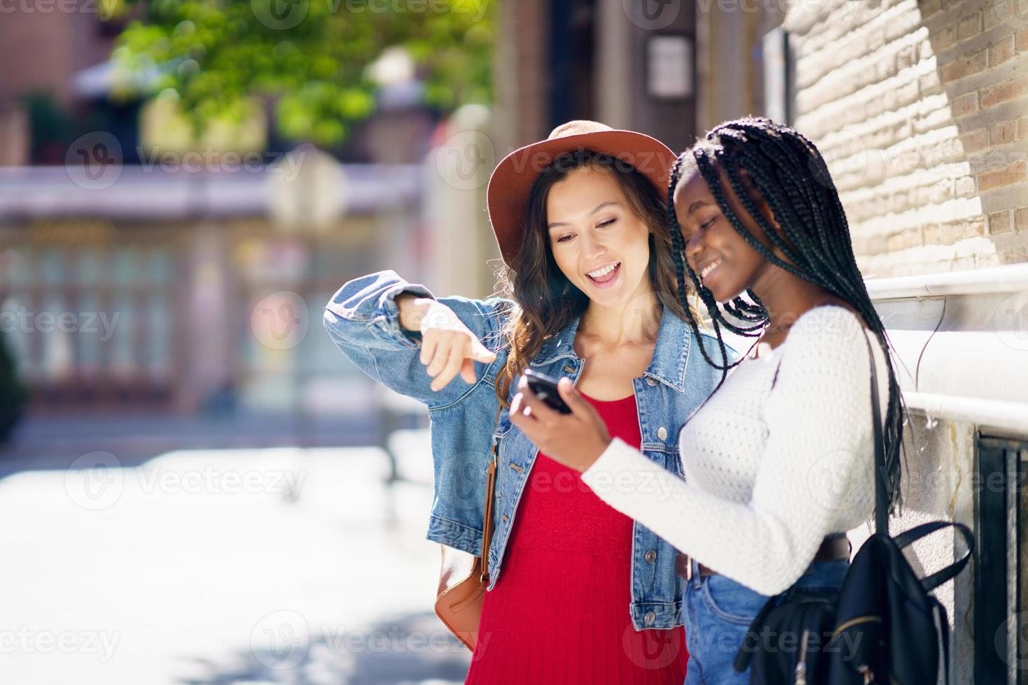 Two friends looking at their smartphone together. Multiethnic women. photo