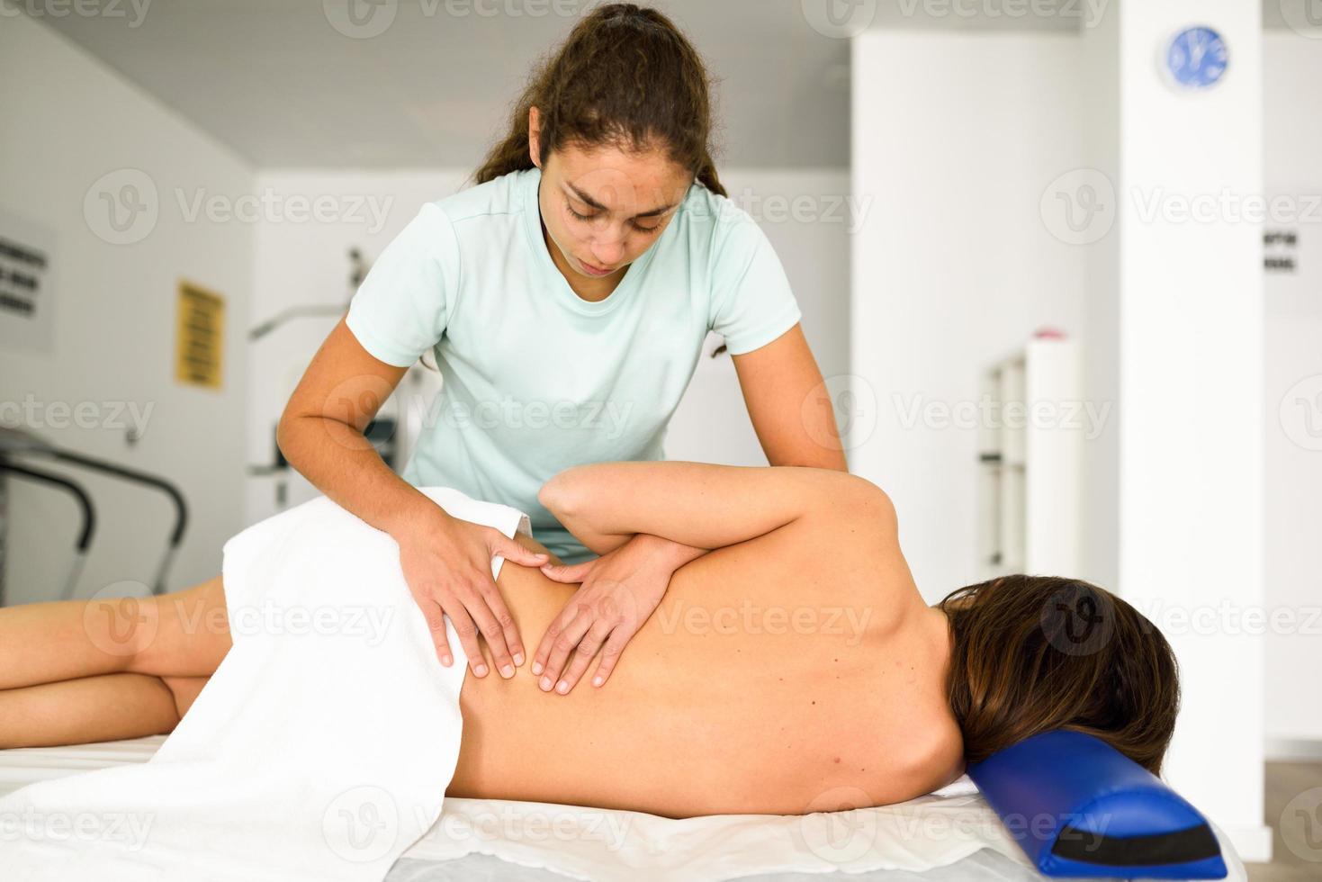 Professional female physiotherapist giving lumbar shoulder massage to a woman photo